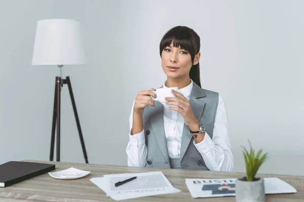 Усміхнена бізнес-леді тримає чашку ізольовано на сірому — стокове фото