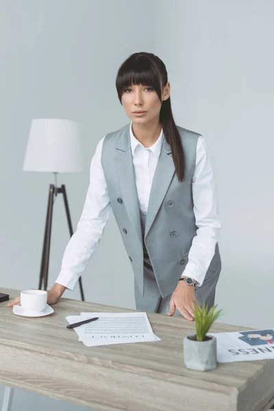 Приваблива бізнес-леді стоїть за столом ізольована на сірому — стокове фото