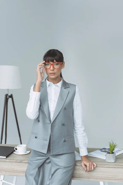 Businesswoman touching glasses and looking at camera isolated on gray — Stock Photo