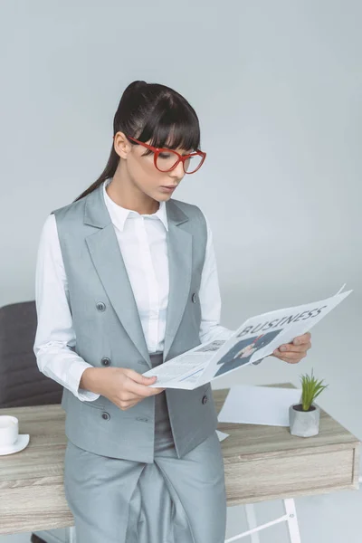 Empresária inclinada na mesa e ler jornal isolado em cinza — Fotografia de Stock
