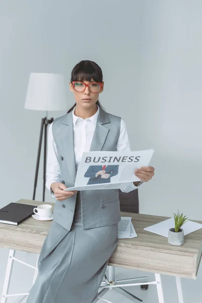 Бізнес-леді тримає газету і дивиться на камеру ізольовано на сірому — стокове фото