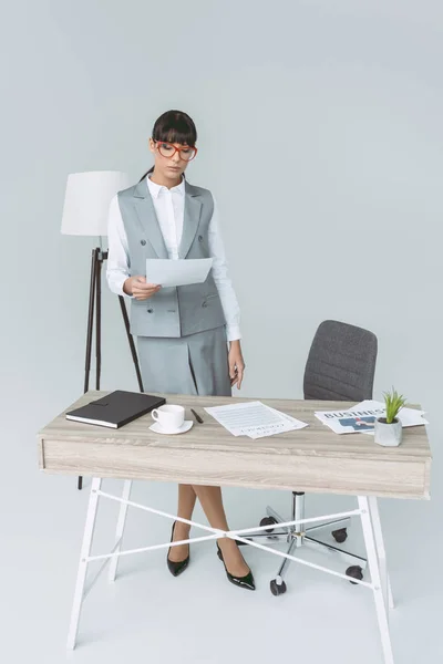 Femme d'affaires debout à table et regardant des documents isolés sur gris — Photo de stock