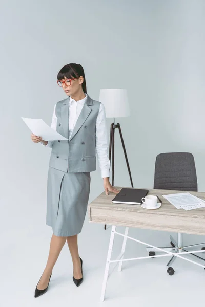 Femme d'affaires debout à table et regardant des documents sur gris — Photo de stock