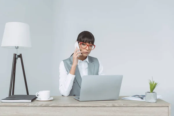 Businesswoman talking by smartphone and using laptop isolated on gray — Stock Photo