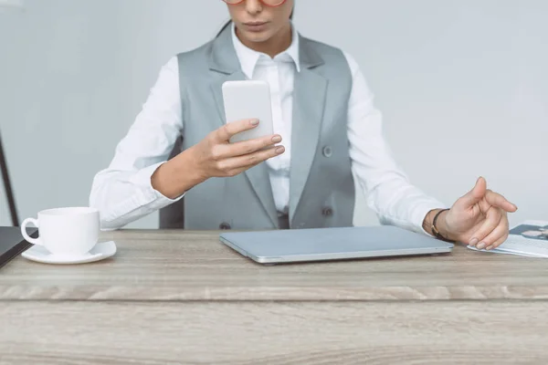 Обрезанный образ деловой женщины, смотрящей на смартфон, изолированный на сером — стоковое фото