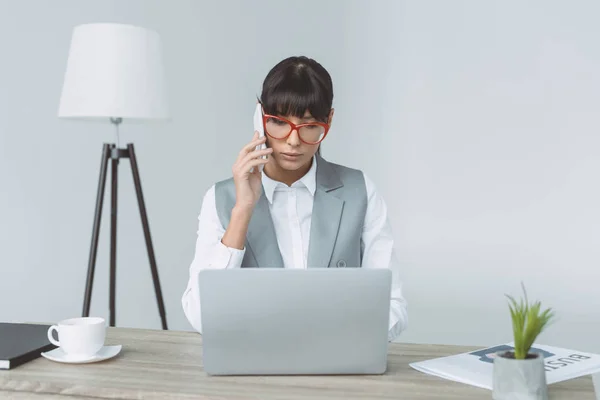 Businesswoman talking by smartphone and using laptop isolated on gray — Stock Photo