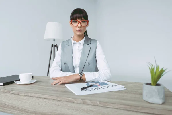 Mujer de negocios sentada en la mesa de trabajo y mirando a la cámara aislada en gris - foto de stock