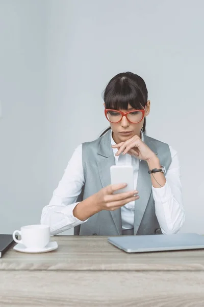 Бізнес-леді дивиться на смартфон ізольовано на сірому — стокове фото