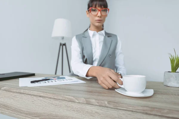 Empresaria tomando taza de café en la mesa aislado en gris - foto de stock