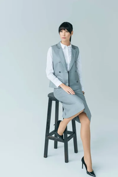 Businesswoman sitting on chair and looking away on gray — Stock Photo