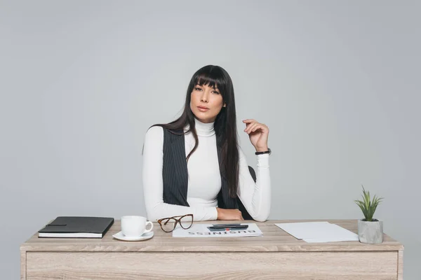 Attraktive brünette Geschäftsfrau sitzt am Arbeitstisch isoliert auf grau — Stockfoto