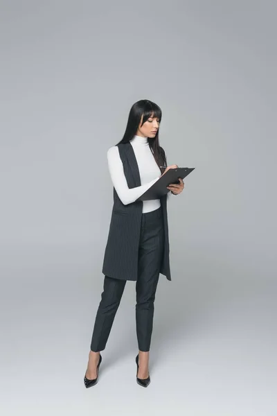 Beautiful businesswoman standing with clipboard on gray — Stock Photo