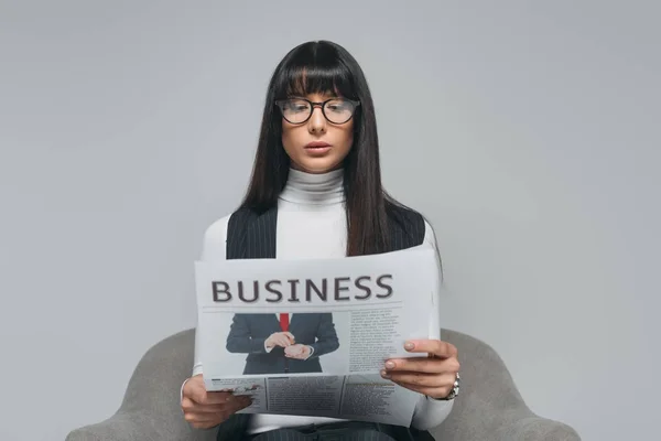 Atractiva morena empresaria leyendo periódico aislado en gris - foto de stock