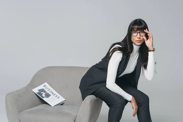 Приваблива брюнетка бізнес-леді сидить на кріслі ізольована на сірому — стокове фото