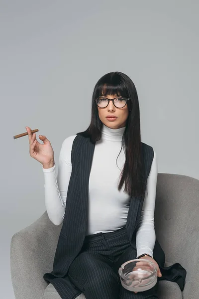 Schöne brünette Geschäftsfrau mit Aschenbecher und Zigarre isoliert auf grau — Stockfoto