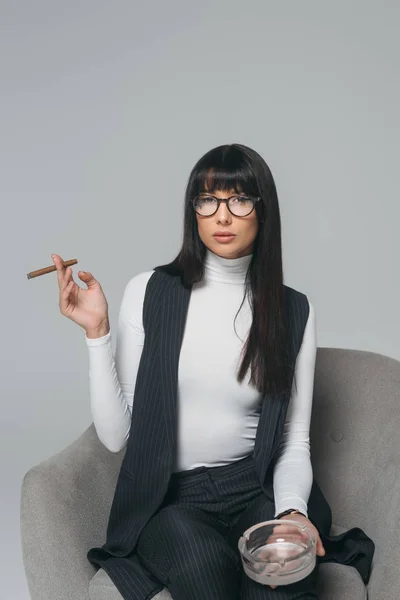 Hermosa morena empresaria con cenicero y cigarro aislado en gris - foto de stock