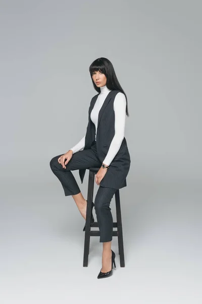 Приваблива брюнетка жінка сидить на чорному стільці на сірому — стокове фото