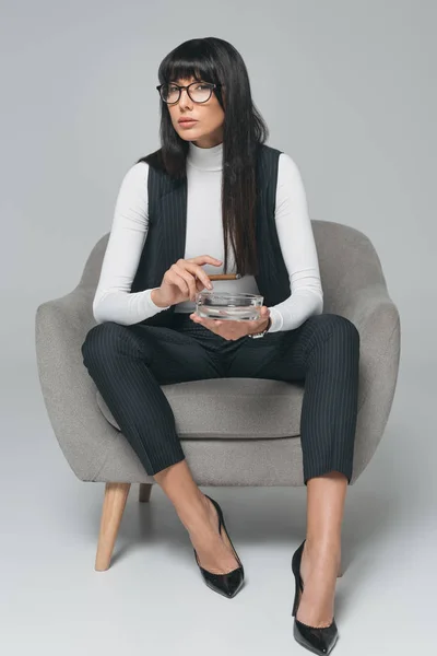 Attractive brunette businesswoman holding ashtray and cigar on gray — Stock Photo