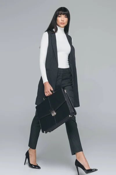 Attractive brunette businesswoman walking with briefcase on gray — Stock Photo