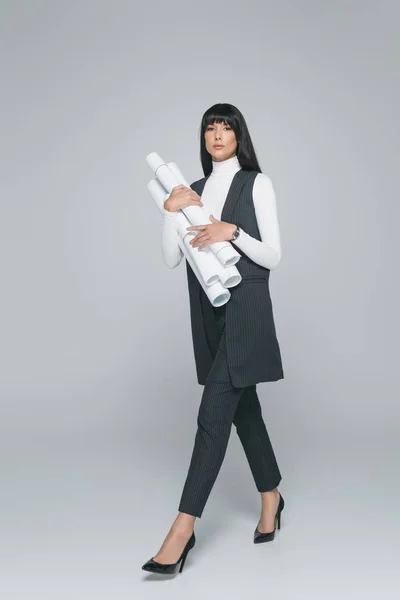 Female architect walking with blueprints on gray — Stock Photo