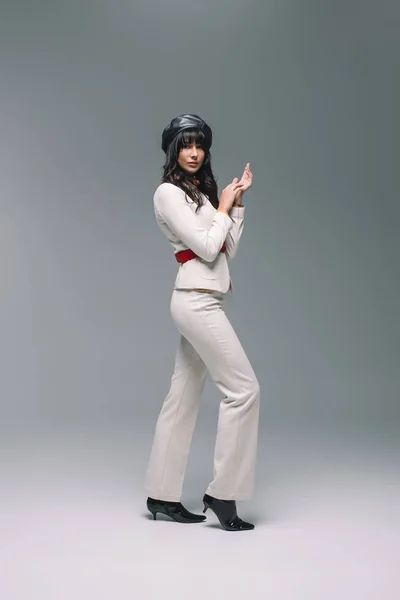 Atractiva mujer morena en traje blanco de pie sobre gris - foto de stock