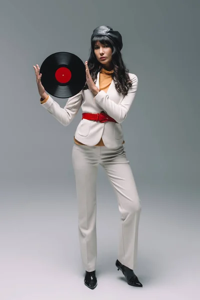 Attractive brunette woman in white suit holding vinyl on gray — Stock Photo