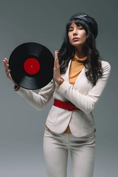 Mulher morena atraente em terno branco segurando vinil isolado em cinza — Fotografia de Stock