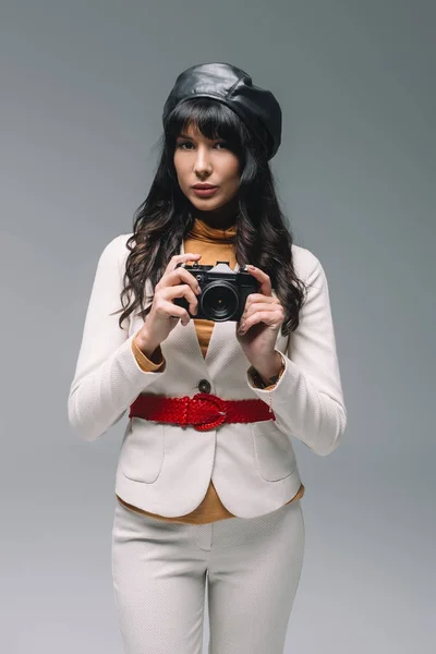 Attrayant brunette femme en costume blanc debout avec caméra de film isolé sur gris — Photo de stock