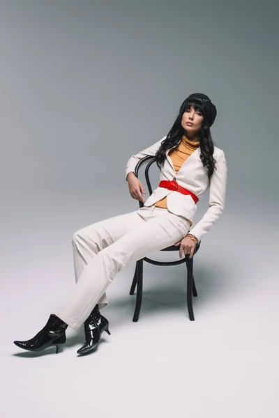 Beautiful brunette woman in white suit lying on chair on gray — Stock Photo