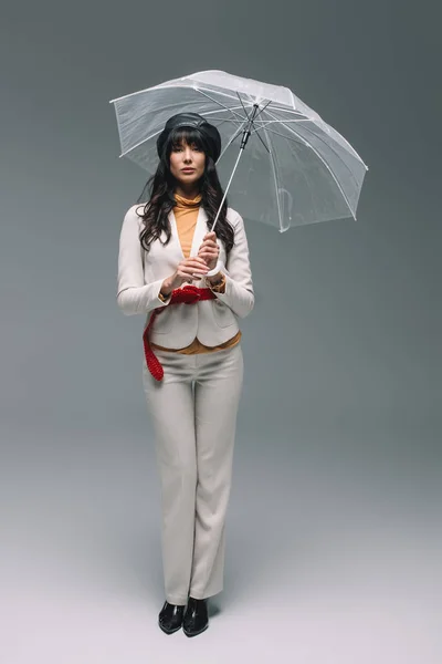 Brunette woman in white suit standing with umbrella on gray — Stock Photo