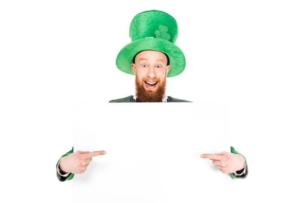 Leprechaun in green suit pointing at blank placard, isolated on white — Stock Photo