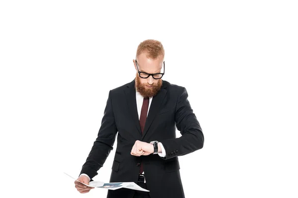 Bearded businessman in eyeglasses holding newspaper and checking wristwatch isolated on white — Stock Photo