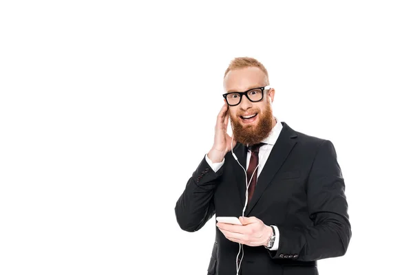 Uomo d'affari barbuto sorridente in cuffia ascoltare musica con smartphone isolato su bianco — Foto stock