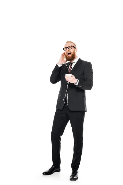 Heureux jeune homme d'affaires dans écouteurs écouter de la musique avec smartphone isolé sur blanc — Photo de stock