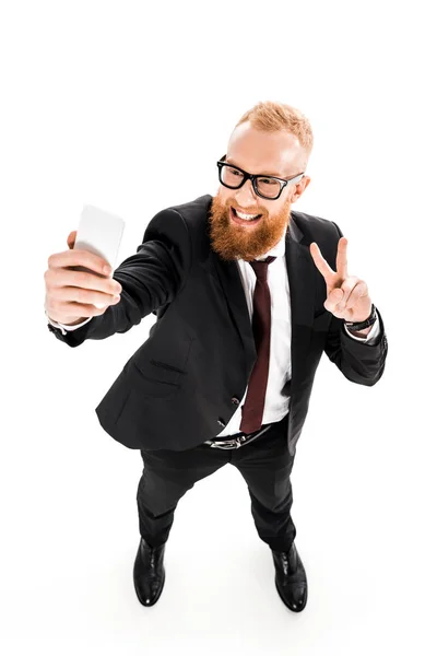 Vista ad alto angolo di uomo d'affari barbuto sorridente scattare selfie con smartphone isolato su bianco — Foto stock