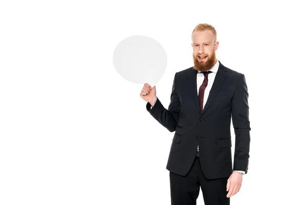 Guapo barbudo hombre de negocios sosteniendo la burbuja del habla en blanco y sonriendo a la cámara aislado en blanco - foto de stock