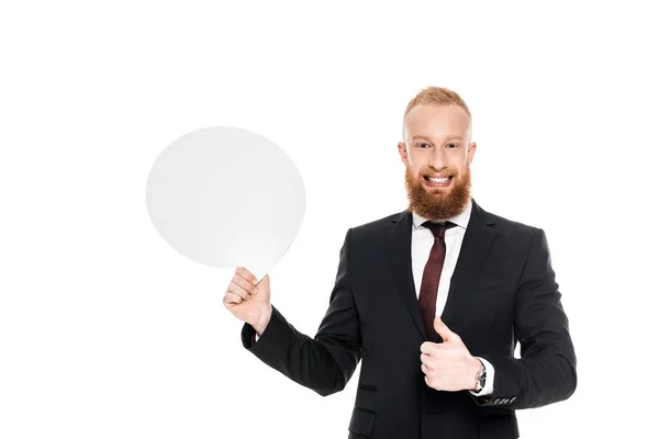 Sonriente hombre de negocios barbudo sosteniendo burbuja de habla en blanco y mostrando el pulgar hacia arriba aislado en blanco - foto de stock