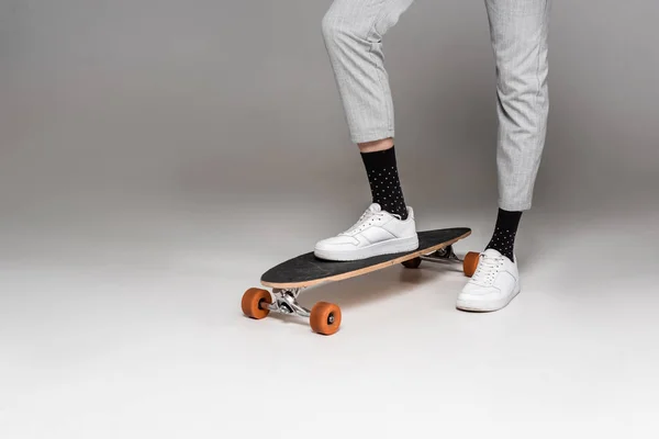 Sezione bassa di uomo alla moda in piedi su skateboard su grigio — Foto stock