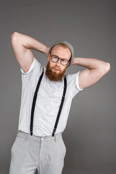 Porträt eines schönen bärtigen Mannes in Hosenträgern, der in die Kamera blickt, während er isoliert auf grau posiert — Stockfoto