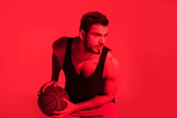 Jeune sportif concentré jouant au basket à la lumière rouge contrastée — Photo de stock