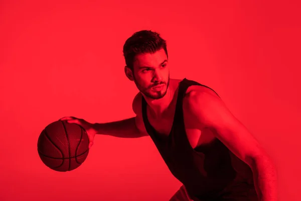 Giovane sportivo concentrato che gioca a basket e guarda lontano a luce rossa a contrasto — Foto stock