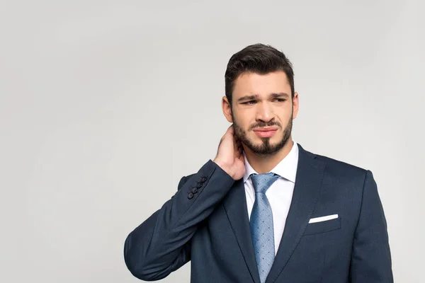 Joven hombre de negocios que sufre de dolor en el cuello y mirando hacia otro lado aislado en gris - foto de stock