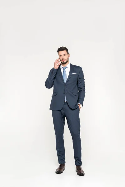 Full length view of stylish young businessman standing with hand in pocket and talking on smartphone isolated on grey — Stock Photo