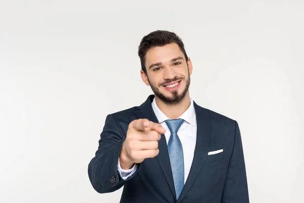 Smiling young businessman pointing at camera isolated on grey — Stock Photo
