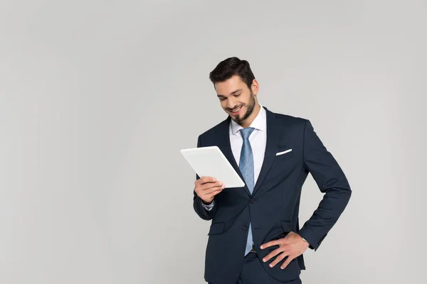 Sonriente joven empresario sosteniendo tableta digital aislada en gris - foto de stock