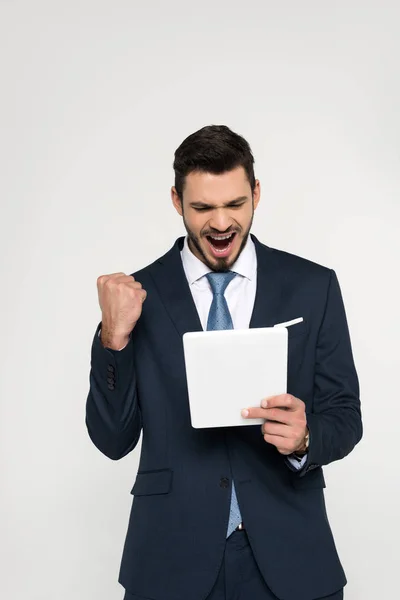 Triumphing young businessman holding digital tablet isolated on grey — Stock Photo