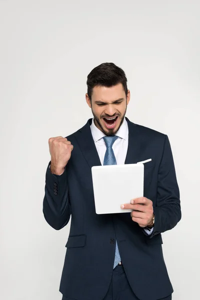 Triumphierender junger Geschäftsmann mit digitalem Tablet isoliert auf grau — Stockfoto