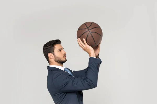 Vue de côté du jeune homme d'affaires jetant ballon de basket isolé sur gris — Photo de stock