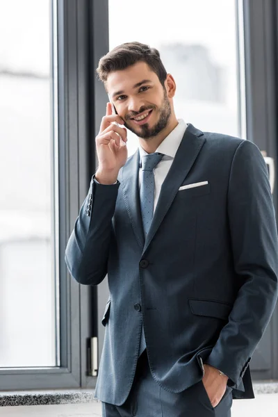 Jungunternehmer spricht mit Smartphone und lächelt im Büro in die Kamera — Stockfoto