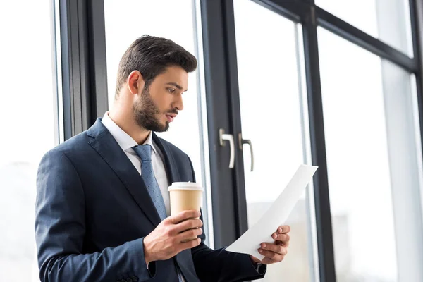 Молодой бизнесмен держит кофе, чтобы пойти и читать газеты в офисе — стоковое фото